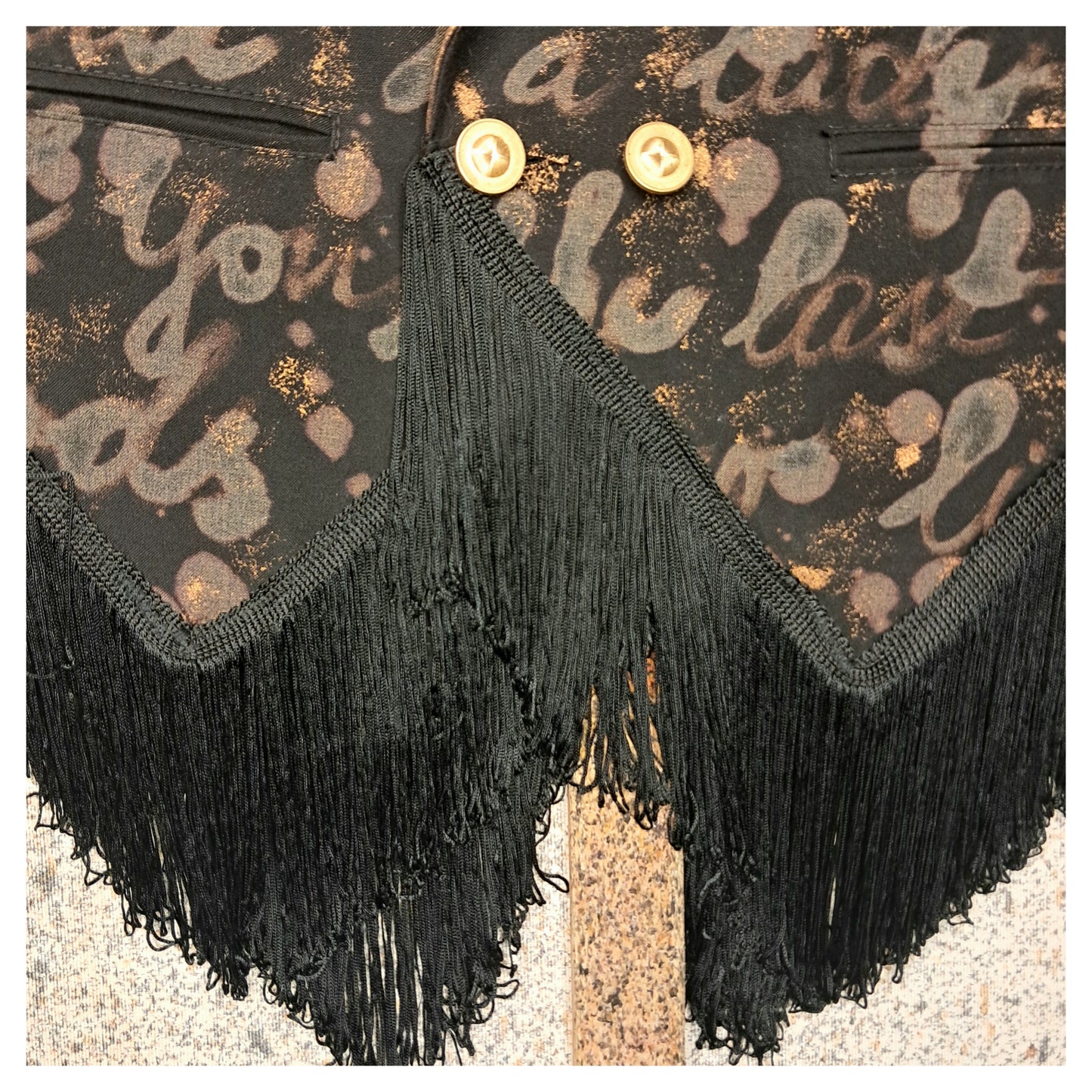Recycled, upcycled tie-dye black and bronze blazer. Lady Gaga’s Abracadabra lyrics hand-painted, tailcoat-style with black ruffle trim.
