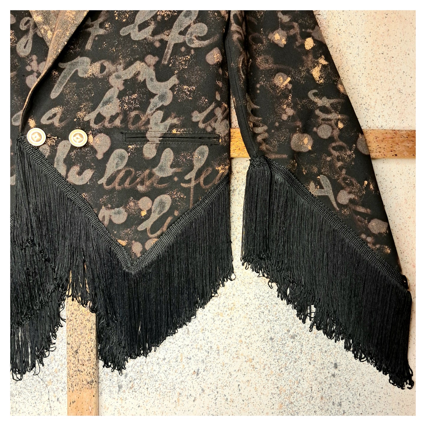 Recycled, upcycled tie-dye black and bronze blazer. Lady Gaga’s Abracadabra lyrics hand-painted, tailcoat-style with black ruffle trim.