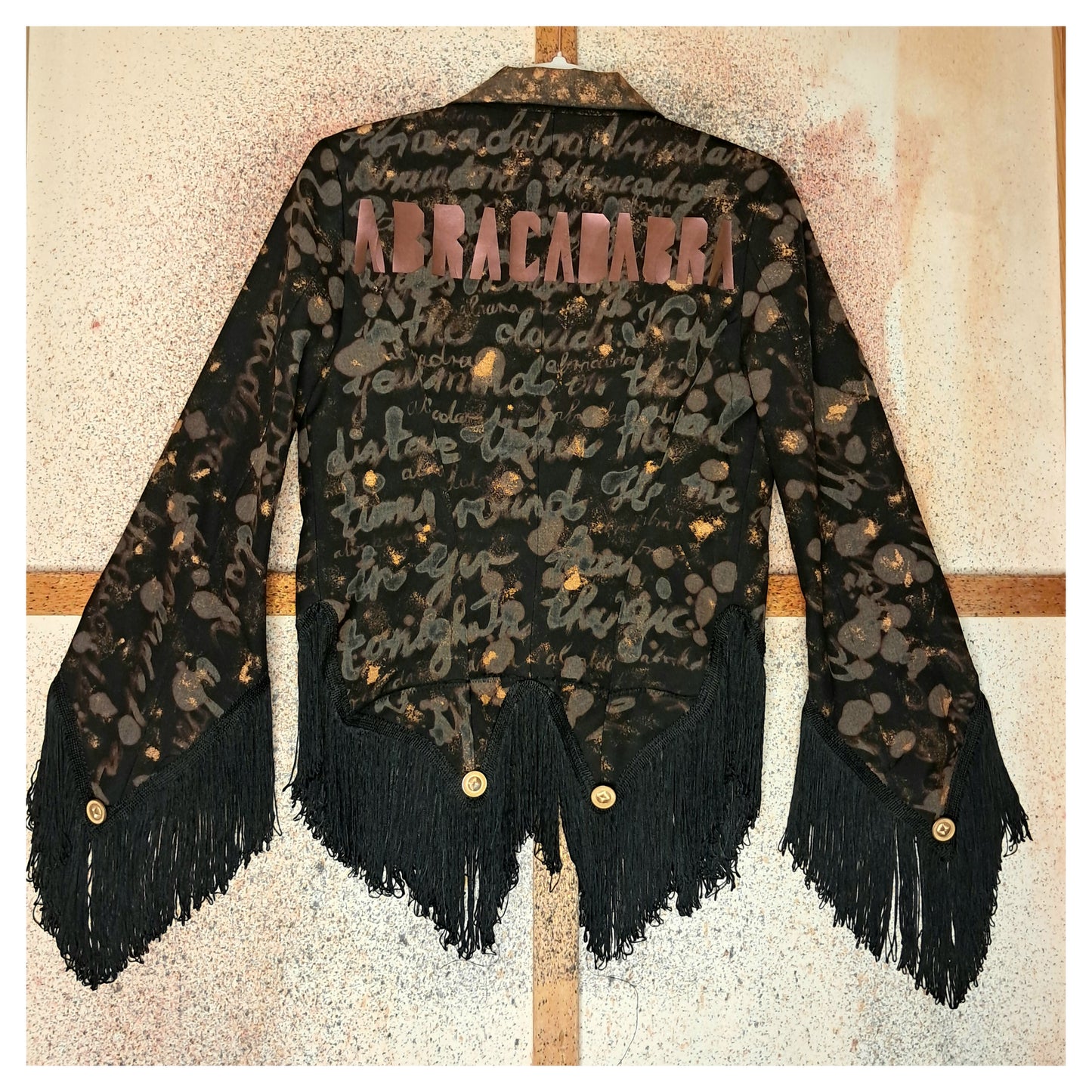 Recycled, upcycled tie-dye black and bronze blazer. Lady Gaga’s Abracadabra lyrics hand-painted, tailcoat-style with black ruffle trim.