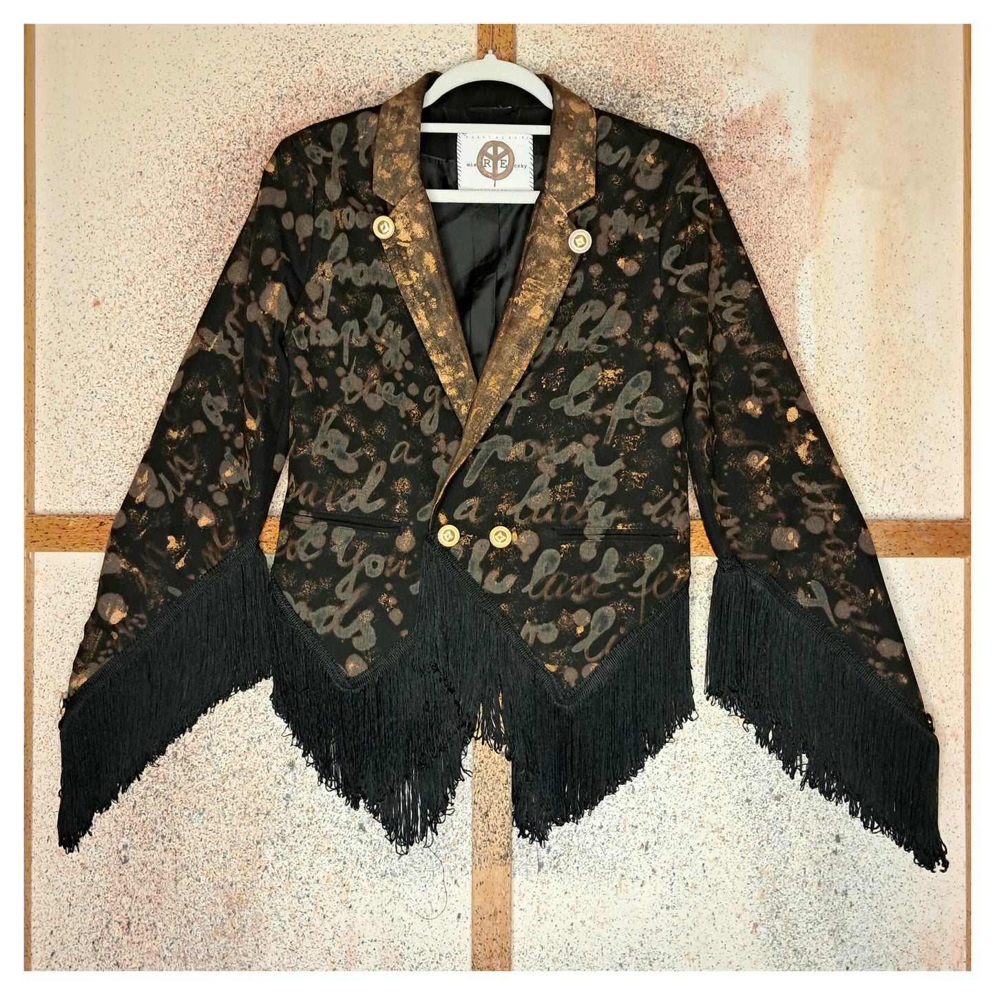 Recycled, upcycled tie-dye black and bronze blazer. Lady Gaga’s Abracadabra lyrics hand-painted, tailcoat-style with black ruffle trim.