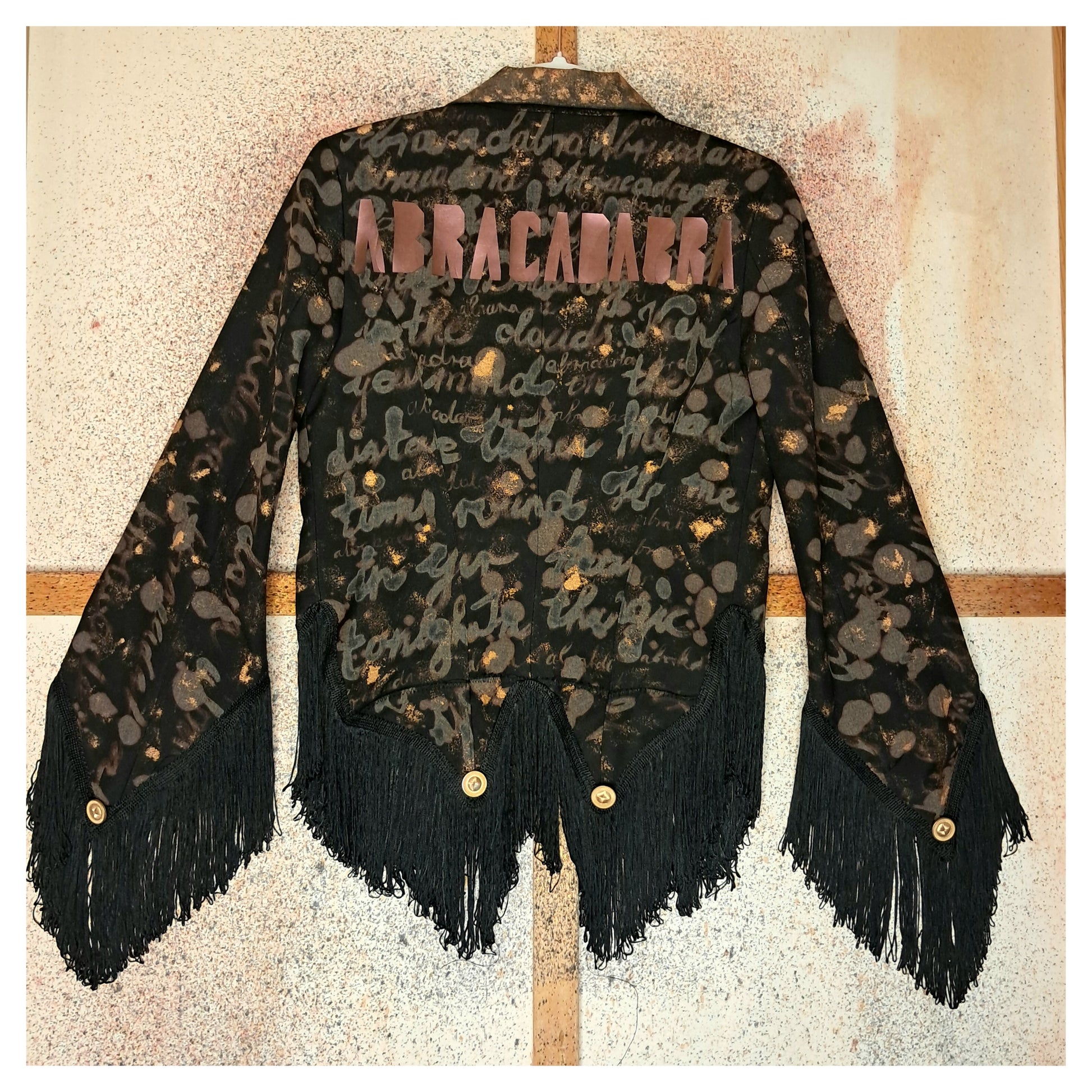 Recycled, upcycled tie-dye black and bronze blazer. Lady Gaga’s Abracadabra lyrics hand-painted, tailcoat-style with black ruffle trim.