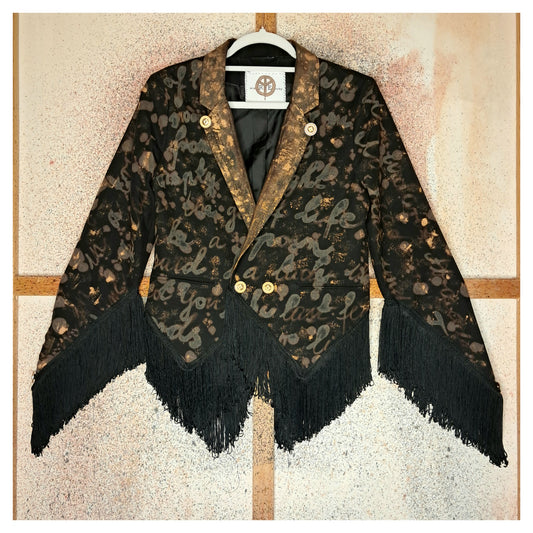Recycled, upcycled tie-dye black and bronze blazer. Lady Gaga’s Abracadabra lyrics hand-painted, tailcoat-style with black ruffle trim.