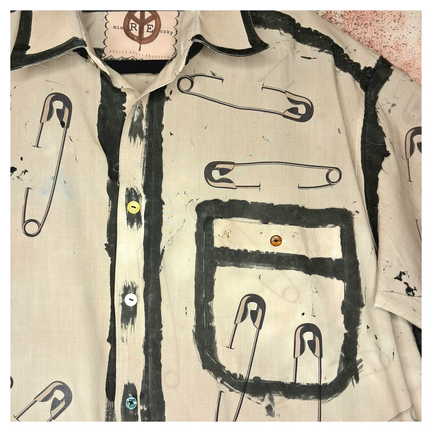 Recycled, upcycled punk beige short-sleeve shirt with safety pin pattern. Handpainted with black fringe and vintage buttons